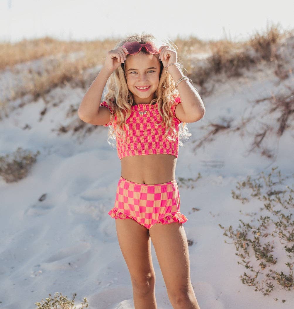 Girl in pink and orange checkered two-piece swimsuit with ruffled bottoms and matching sunglasses.