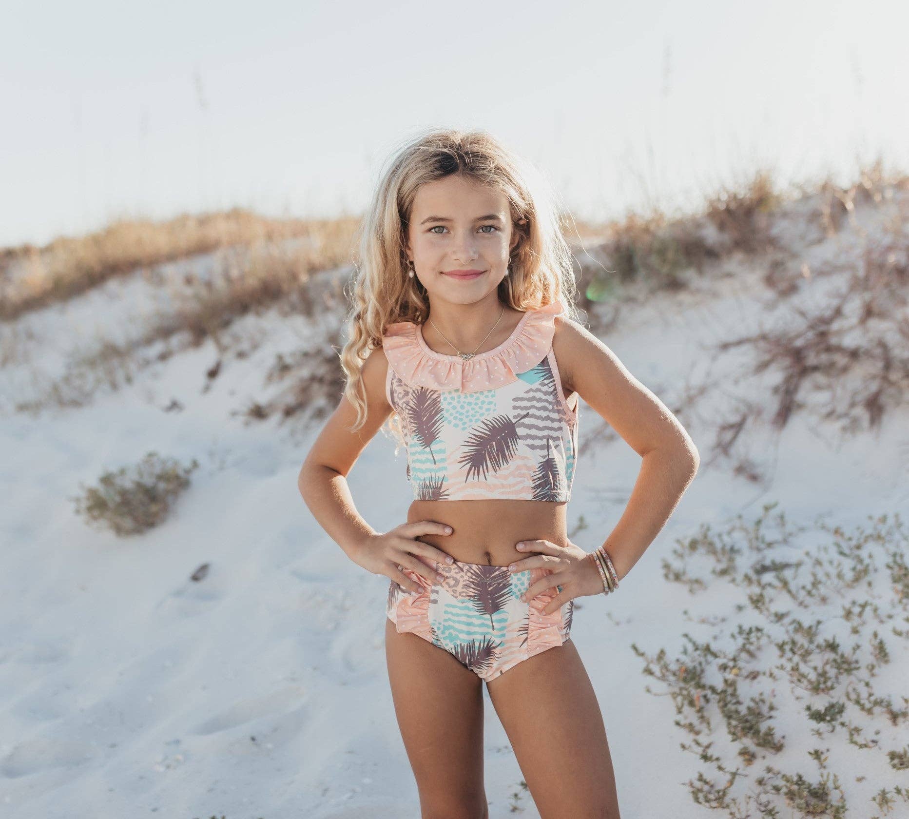 Girl in palm print two-piece swimsuit with ruffle trim on beach