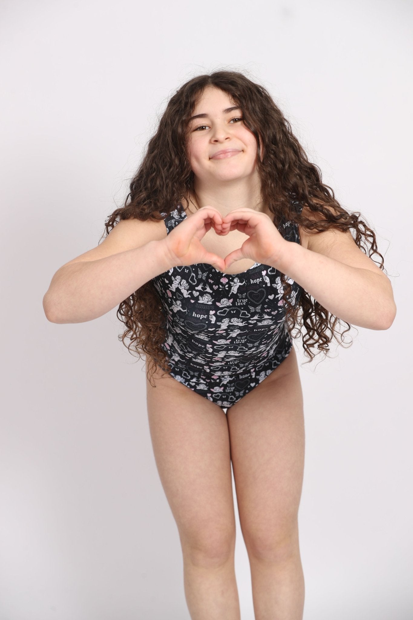 Girl in black & white Cupid print leotard making a heart shape with her hands.