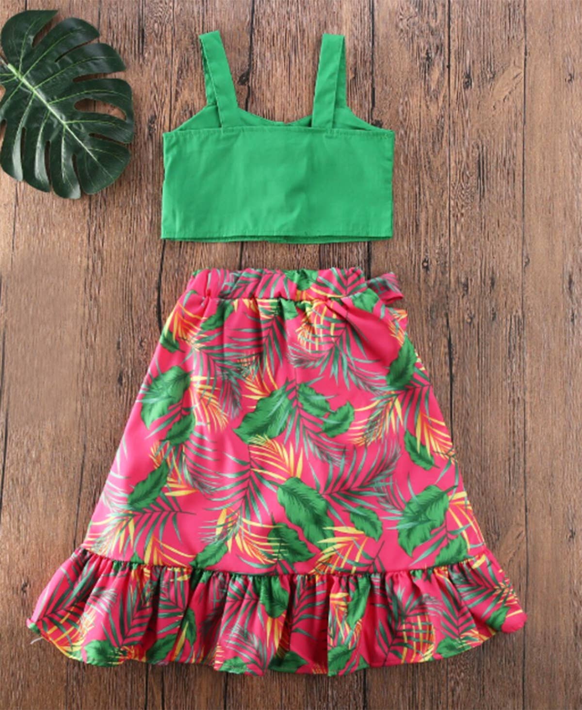 Green crop top and pink tropical print skirt on a wooden surface with a leaf decoration.