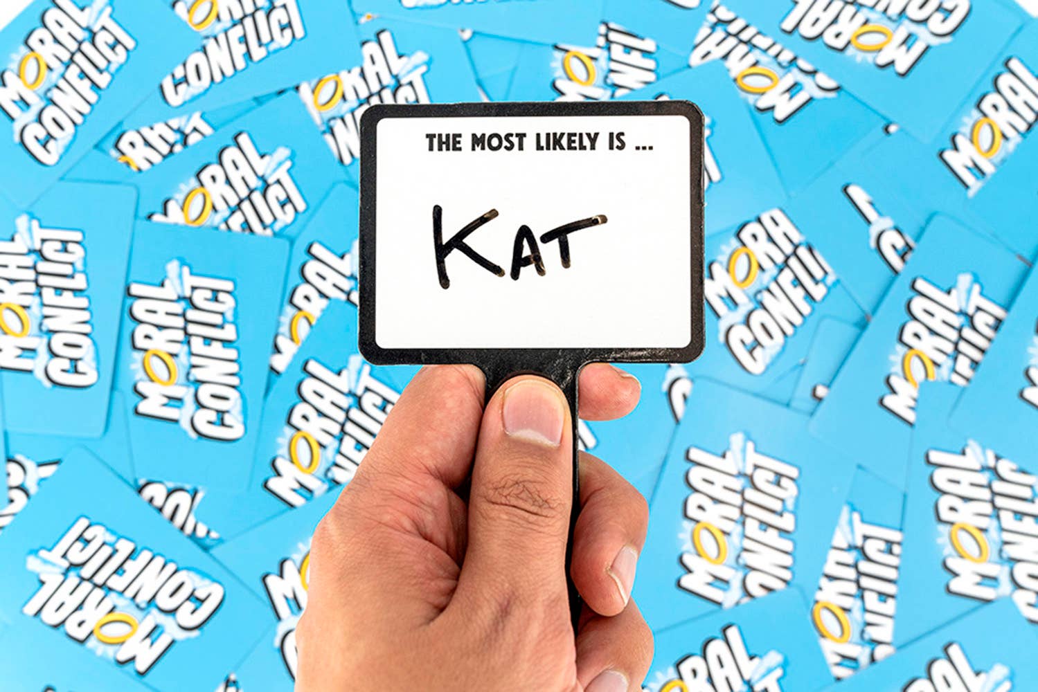 Hand holding a card with 'KAT' on it against a background of 'Moral Conflict' cards.