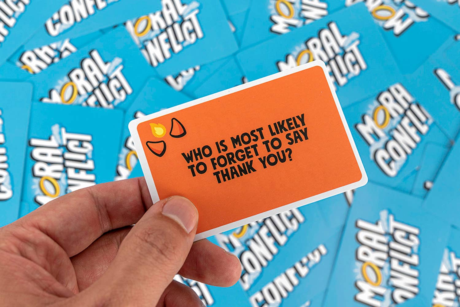 Hand holding a card from 'Moral Conflict' game with text and question, surrounded by more cards.
