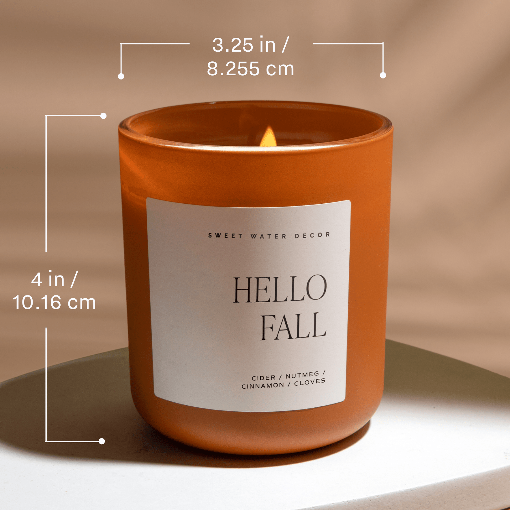 Candle with 'Hello Fall' label and dimensions on a neutral background