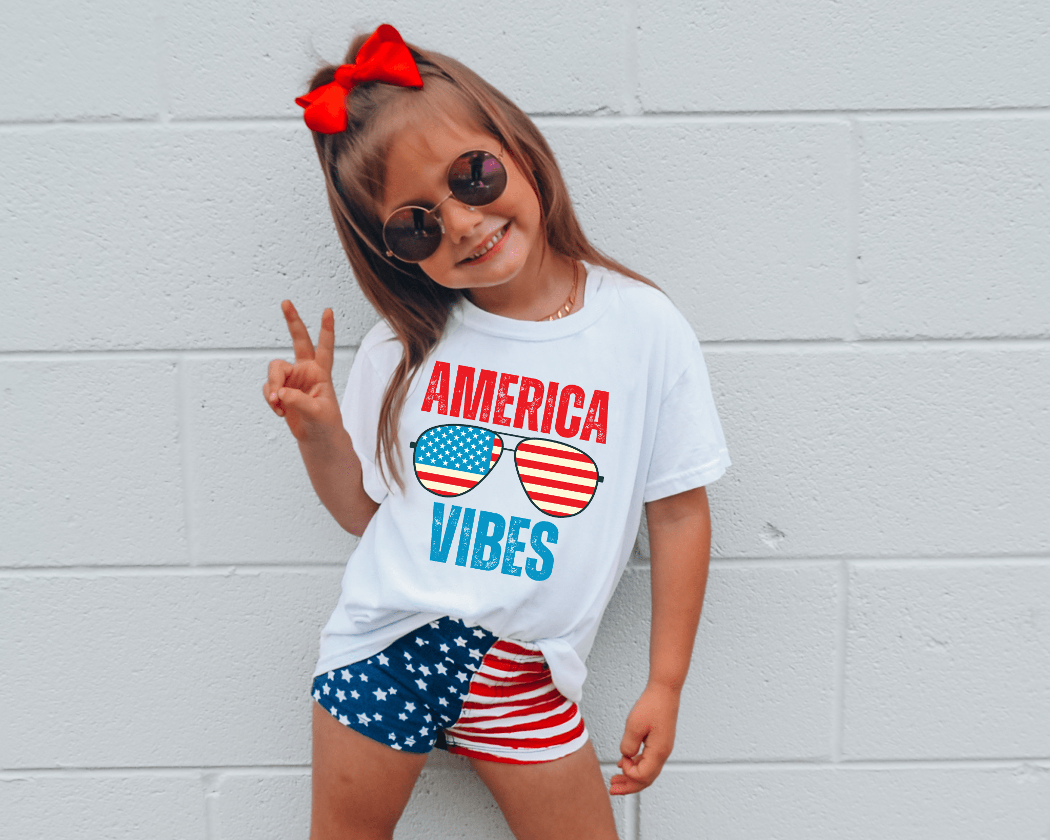 Girl in 'America Vibes' shirt and patriotic shorts, celebrating the Fourth of July.