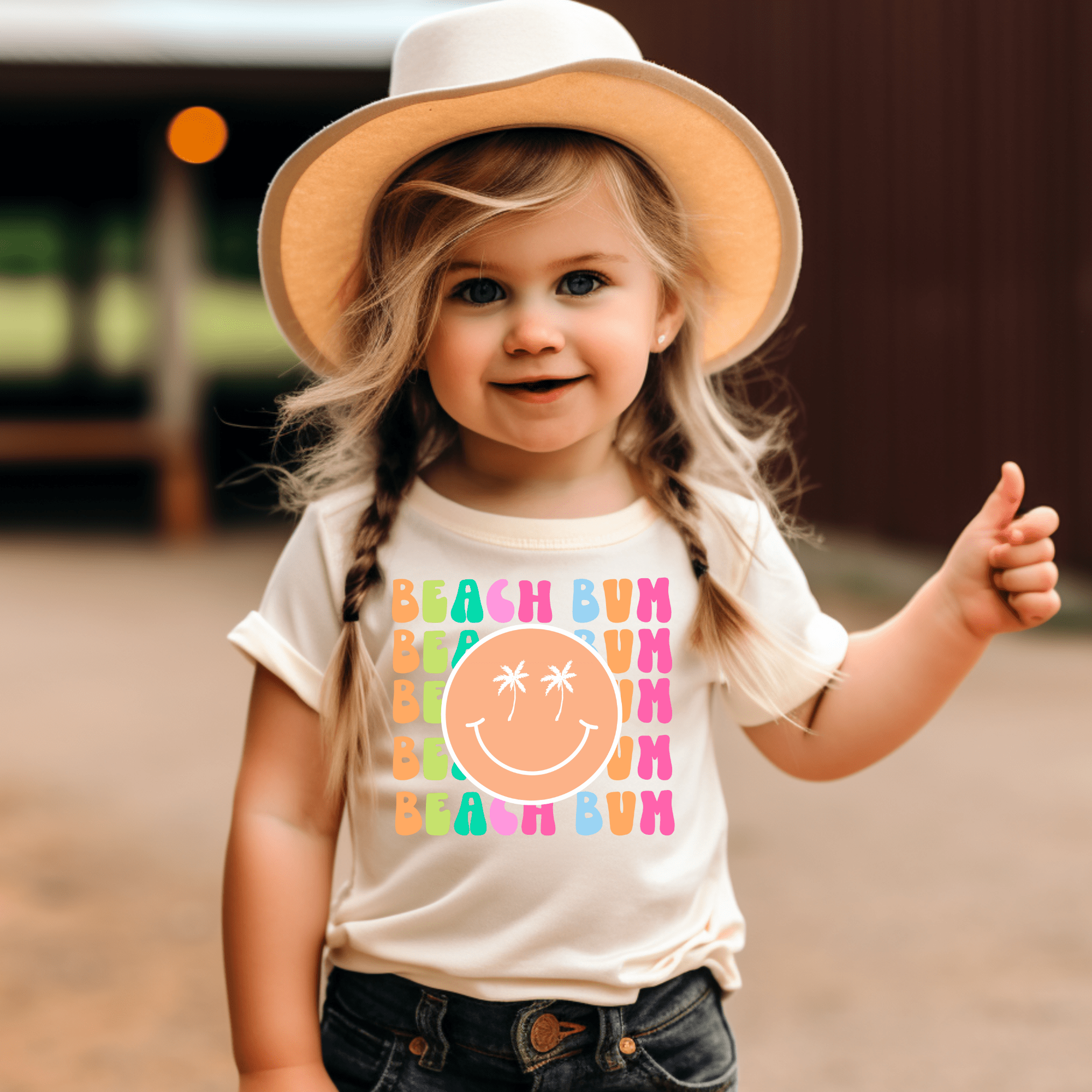 Girl wearing a 'Beach Bum' t-shirt with palm tree graphic and giving thumbs up.