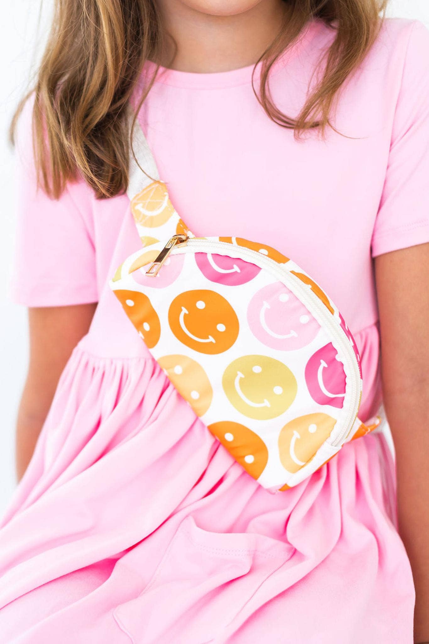 Girl in pink dress with smiley face fanny pack worn across chest.