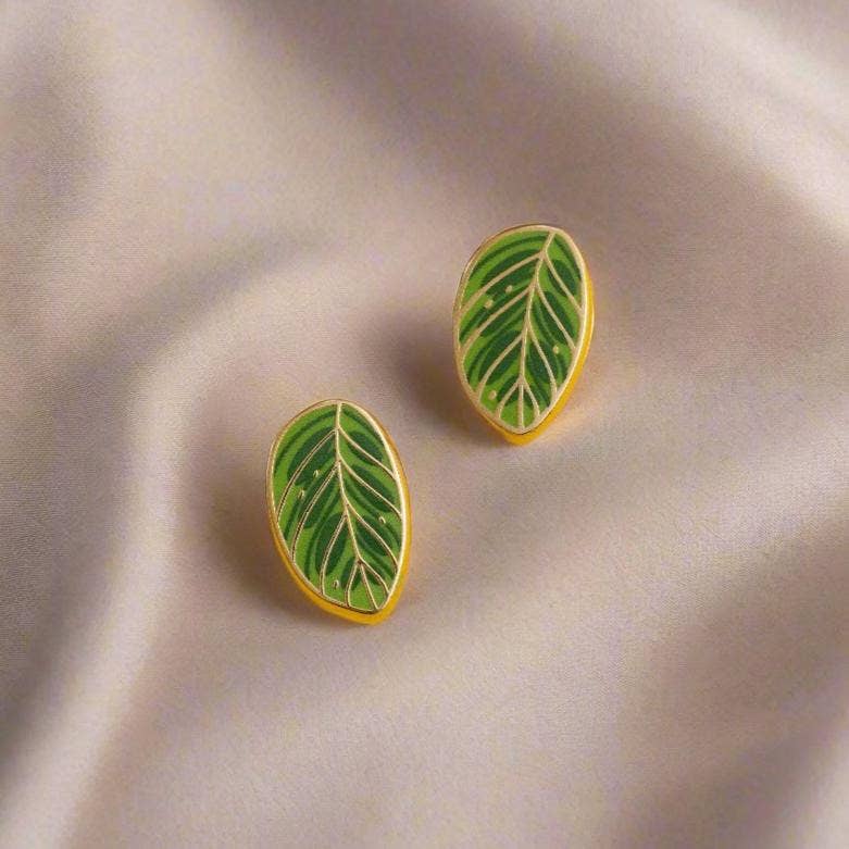 Green leaf-shaped makoyan earrings on a beige fabric background