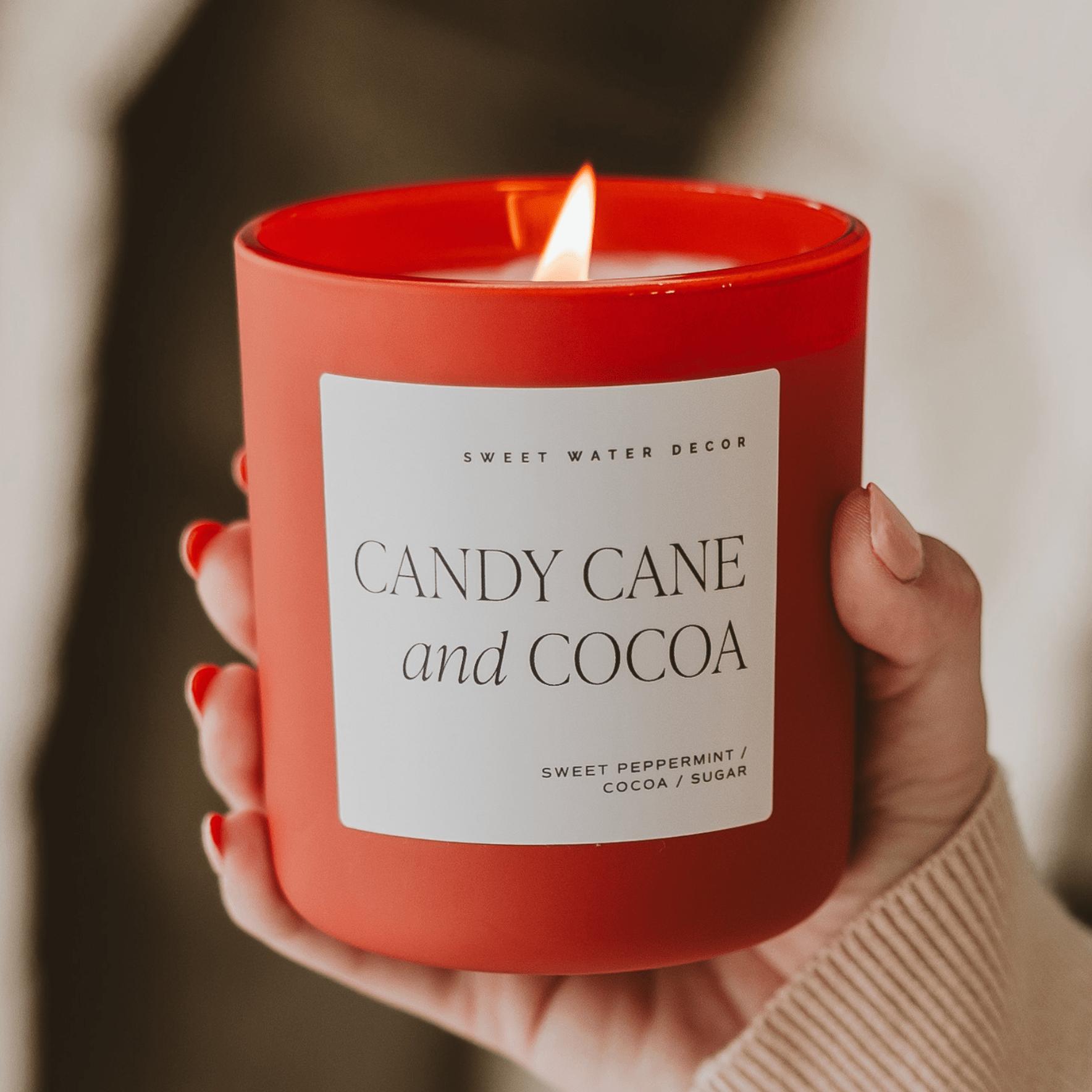 Red candle labeled 'Candy Cane and Cocoa' held by a person with a blurred background