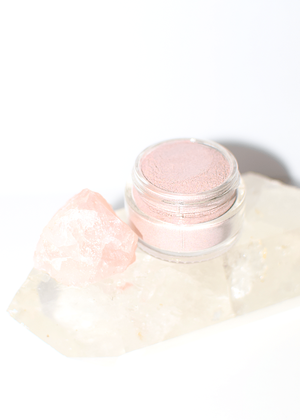 Pink mineral highlighting makeup in a jar with a rose quartz crystal accent.
