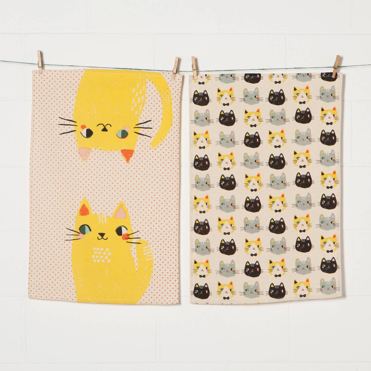 Two cat-themed tea towels hanging on a line against a white background