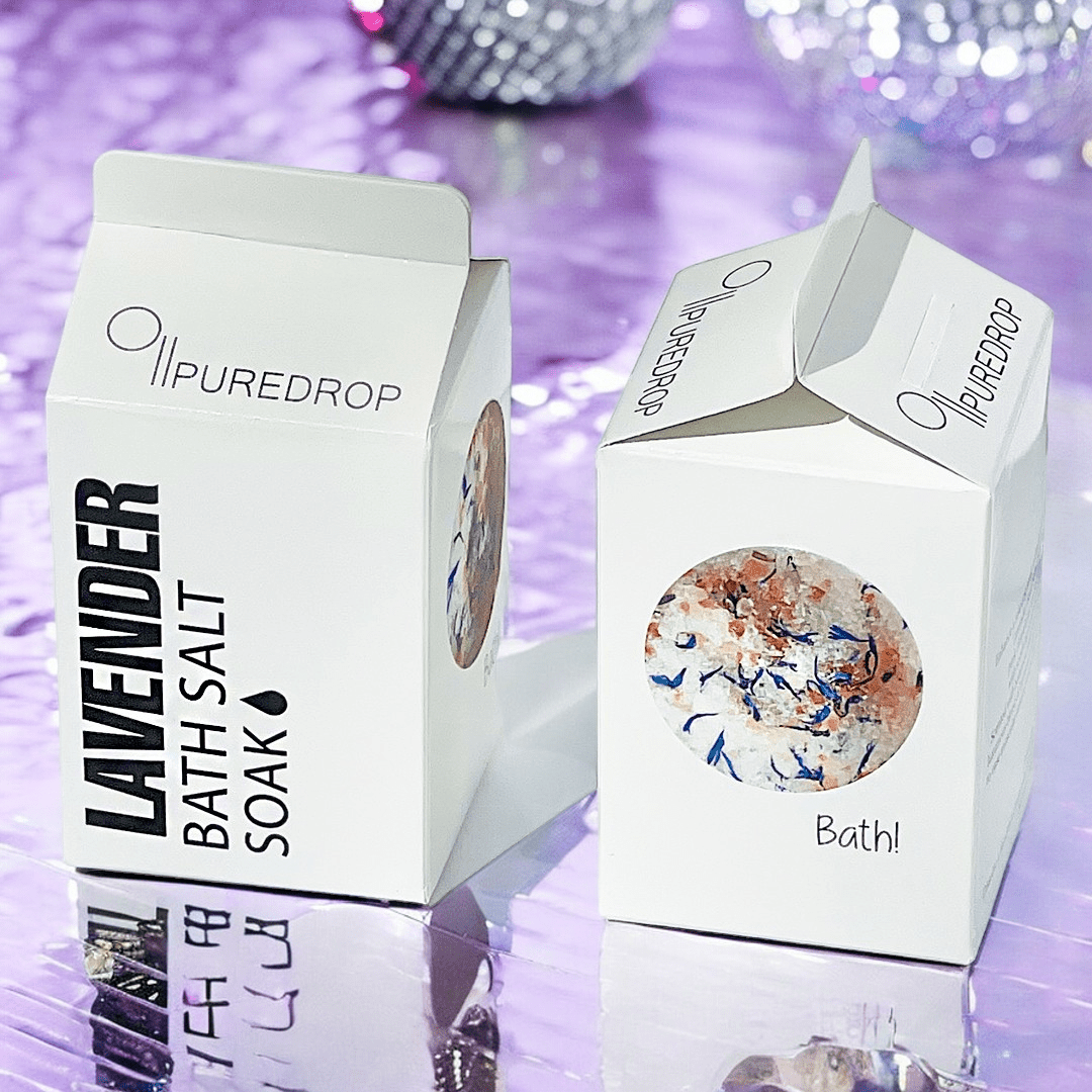 Two white PUREDROP Lavender Bath Salt Soak boxes, milk carton-shaped, showing botanical salts on purple.