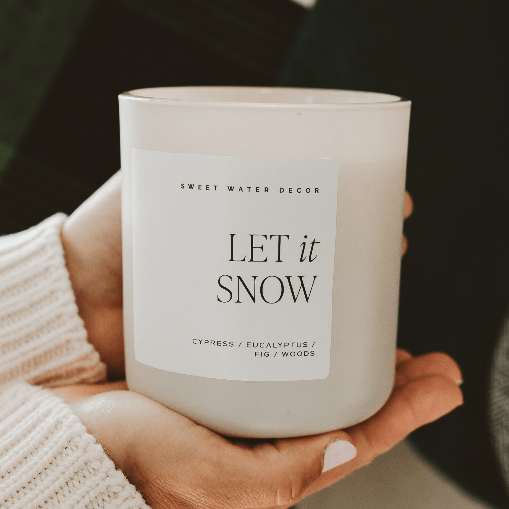 Candle labeled 'Let it Snow' by Sweet Water Decor held in a hand.