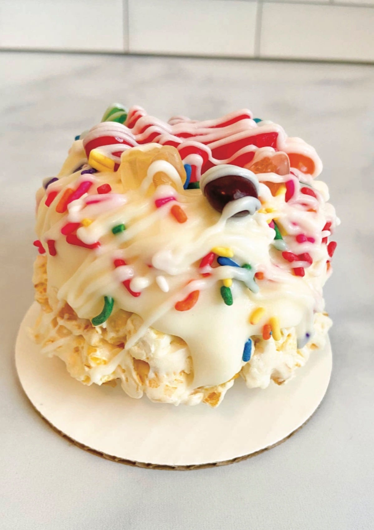 Colorful dessert with popcorn, sprinkles, and candy on a white plate.