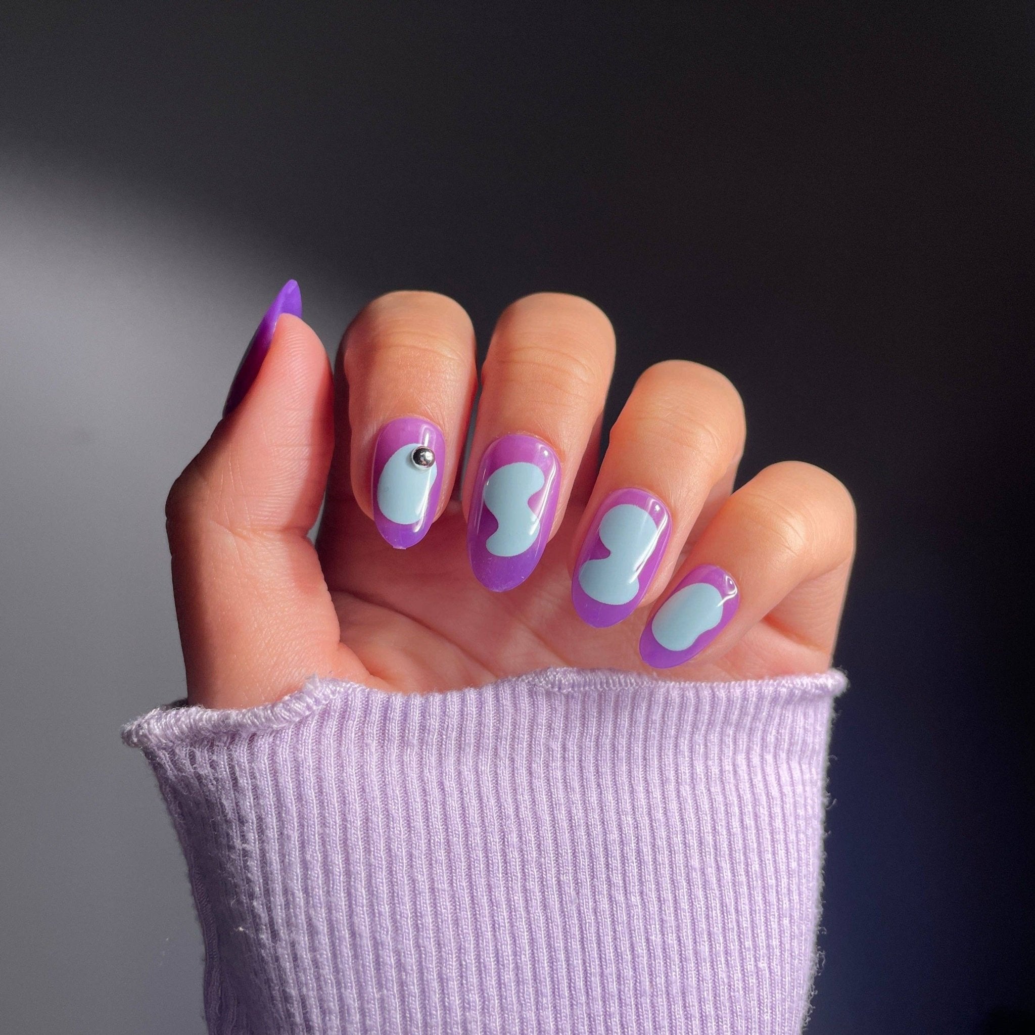 Almond purple press-on nails with light blue abstract design.