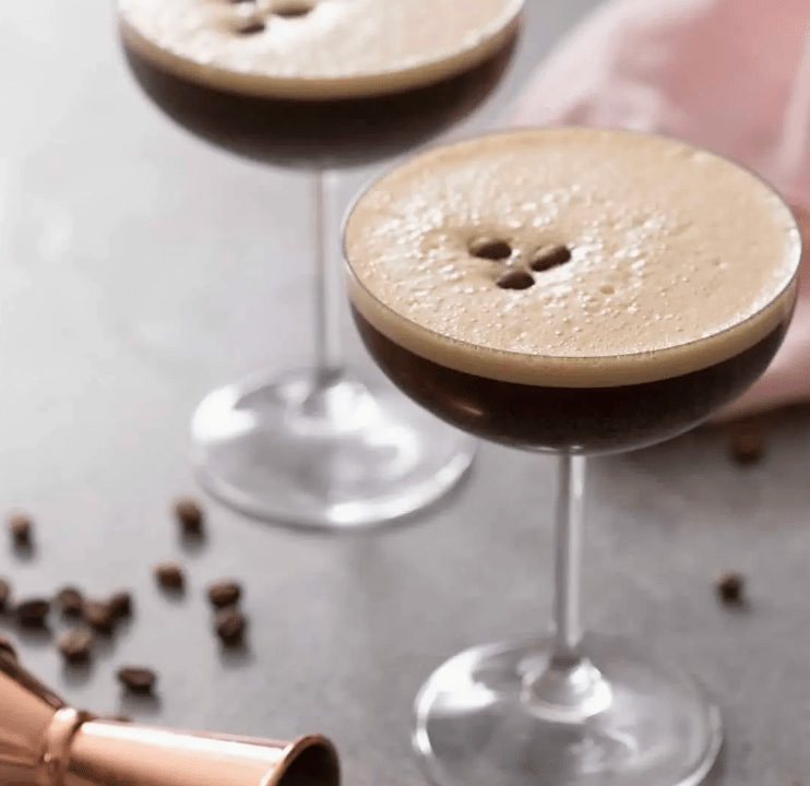 Two espresso martini cocktails in stemmed glasses, garnished with coffee beans.