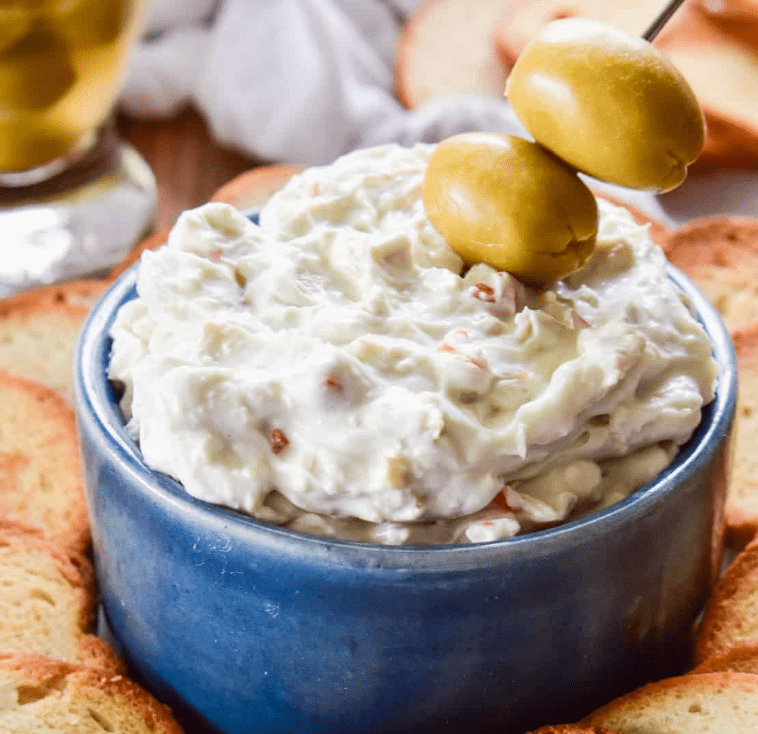 Bowl of olive dip with two olives on top, surrounded by toasted bread slices.