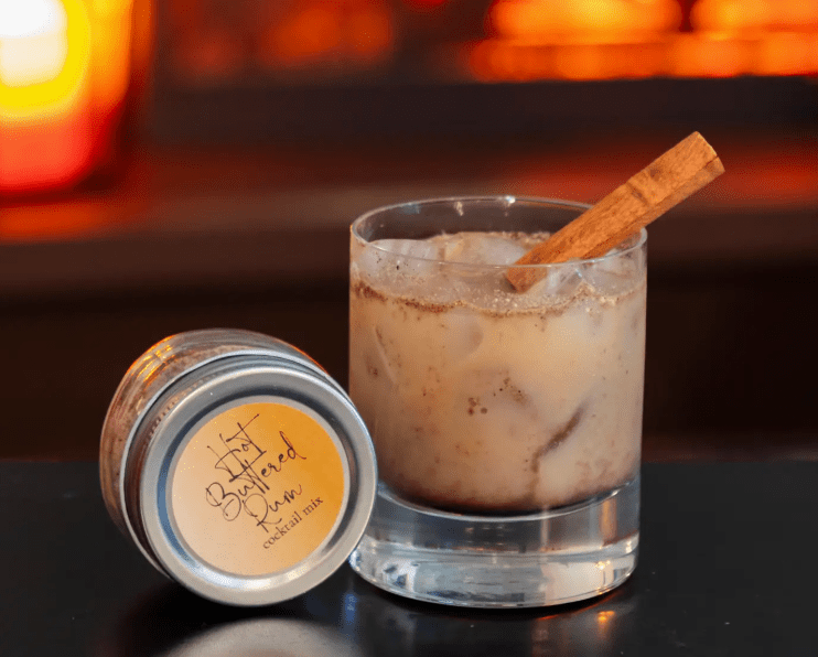 Hot Buttered Rum cocktail mix jar next to a glass with a cinnamon stick.