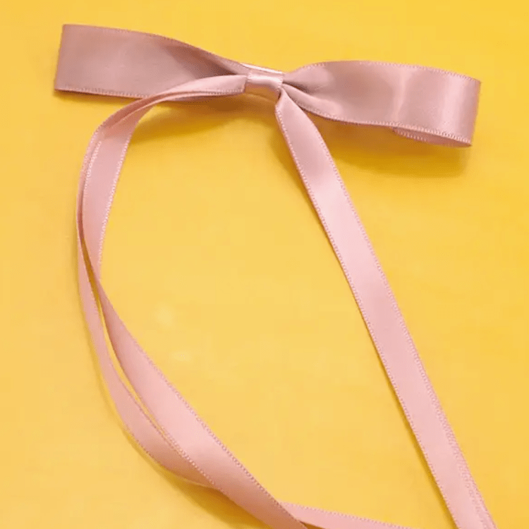Pale pink satin ribbon tied in a bow against a yellow background.