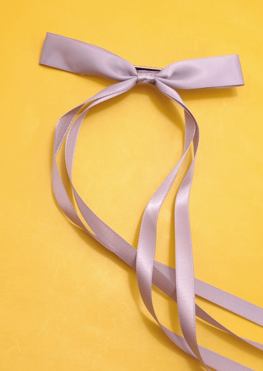Lilac satin ribbon bow and streamers against a yellow background.