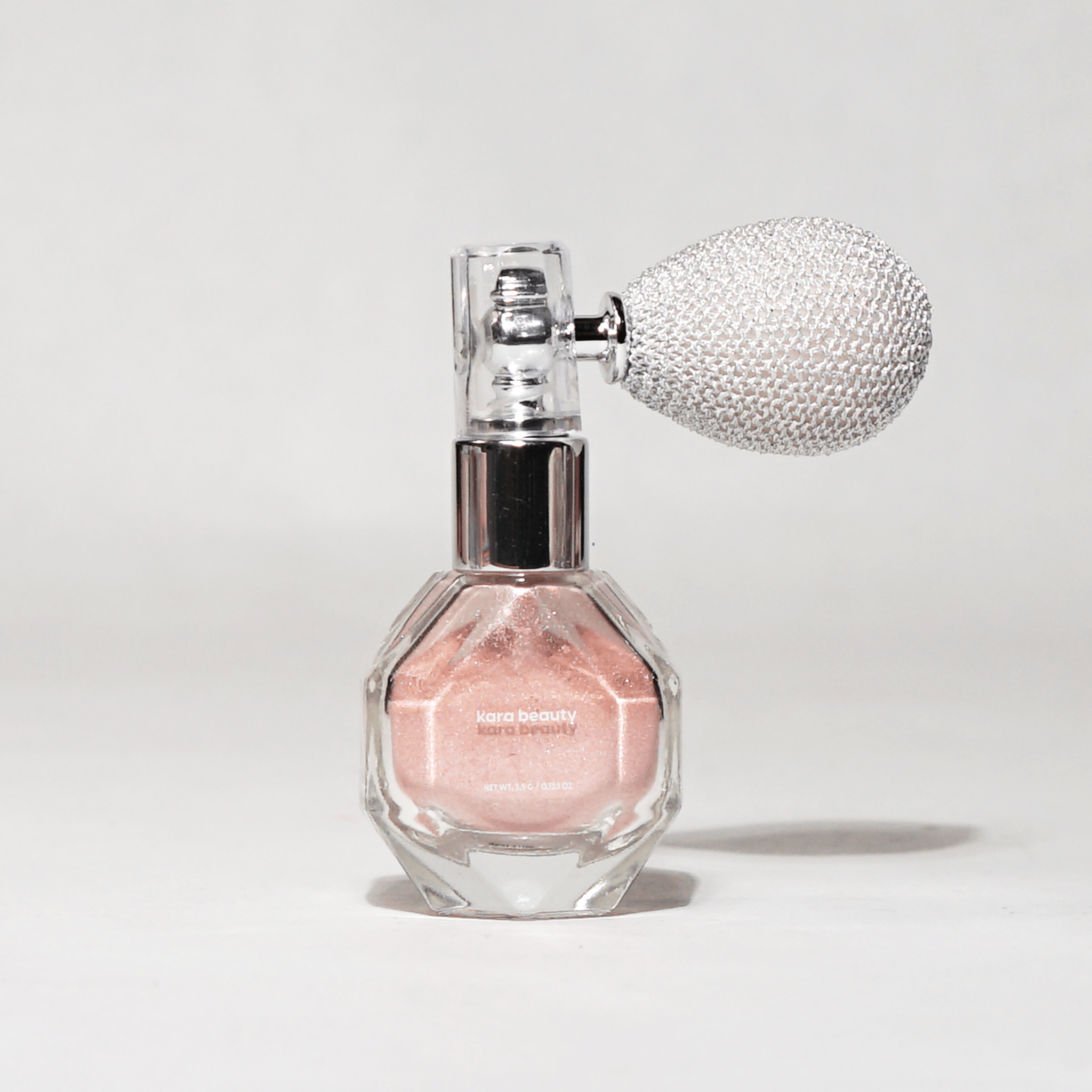 Kara Beauty shimmer spray in a clear glass bottle with a silver bulb atomizer.