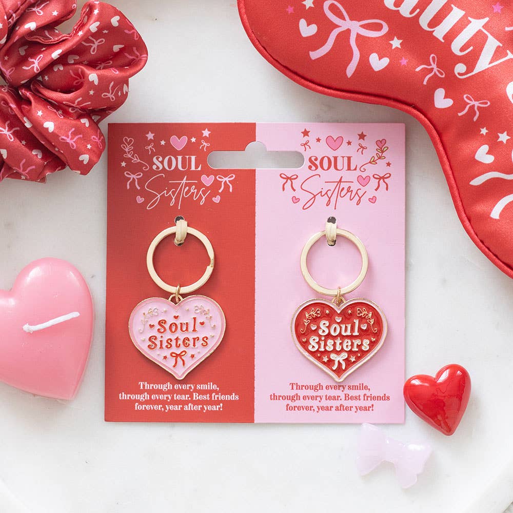 Two 'Soul Sisters' keychains on their packaging with decorative hearts and a red pouch in the background.
