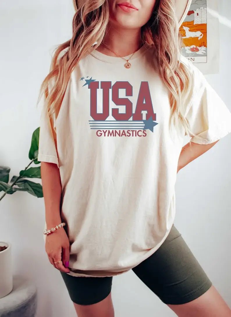 Person wearing a 'USA Gymnastics' t-shirt with a white background