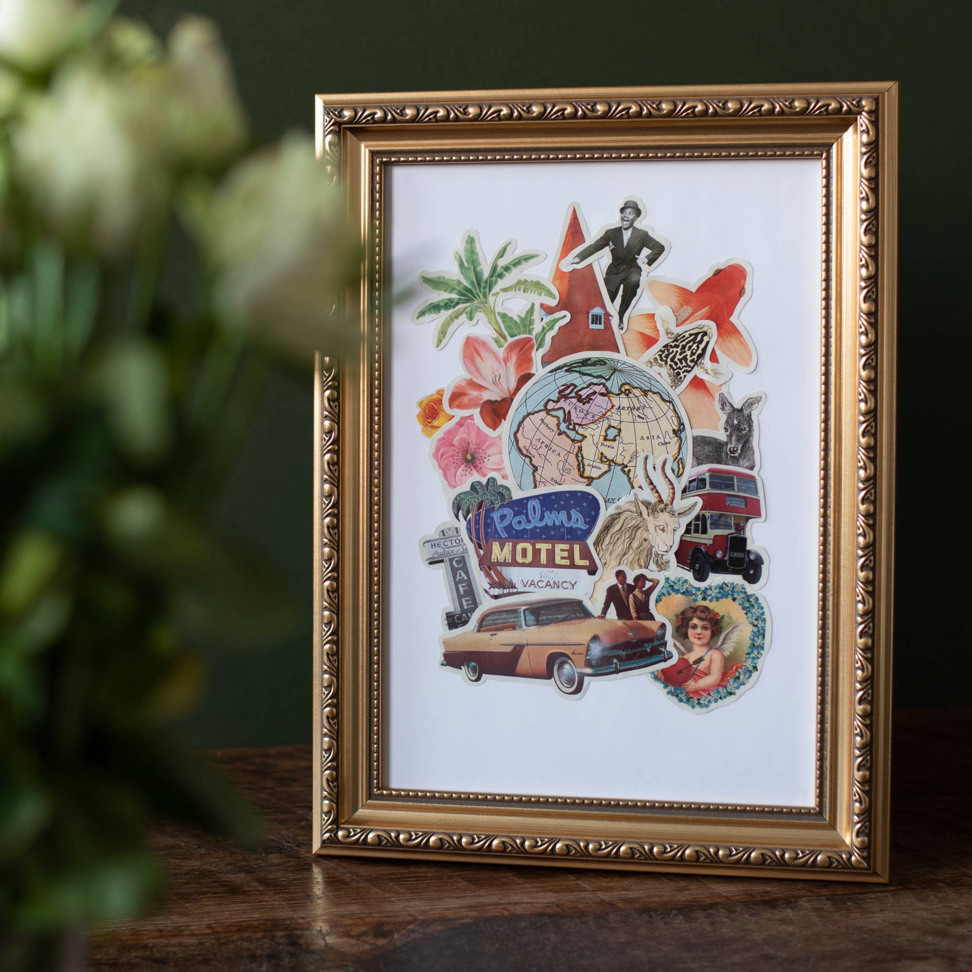Framed collage art featuring travel-themed stickers, including a globe, classic car, and 'Palms Motel' sign, in a gold ornate frame.