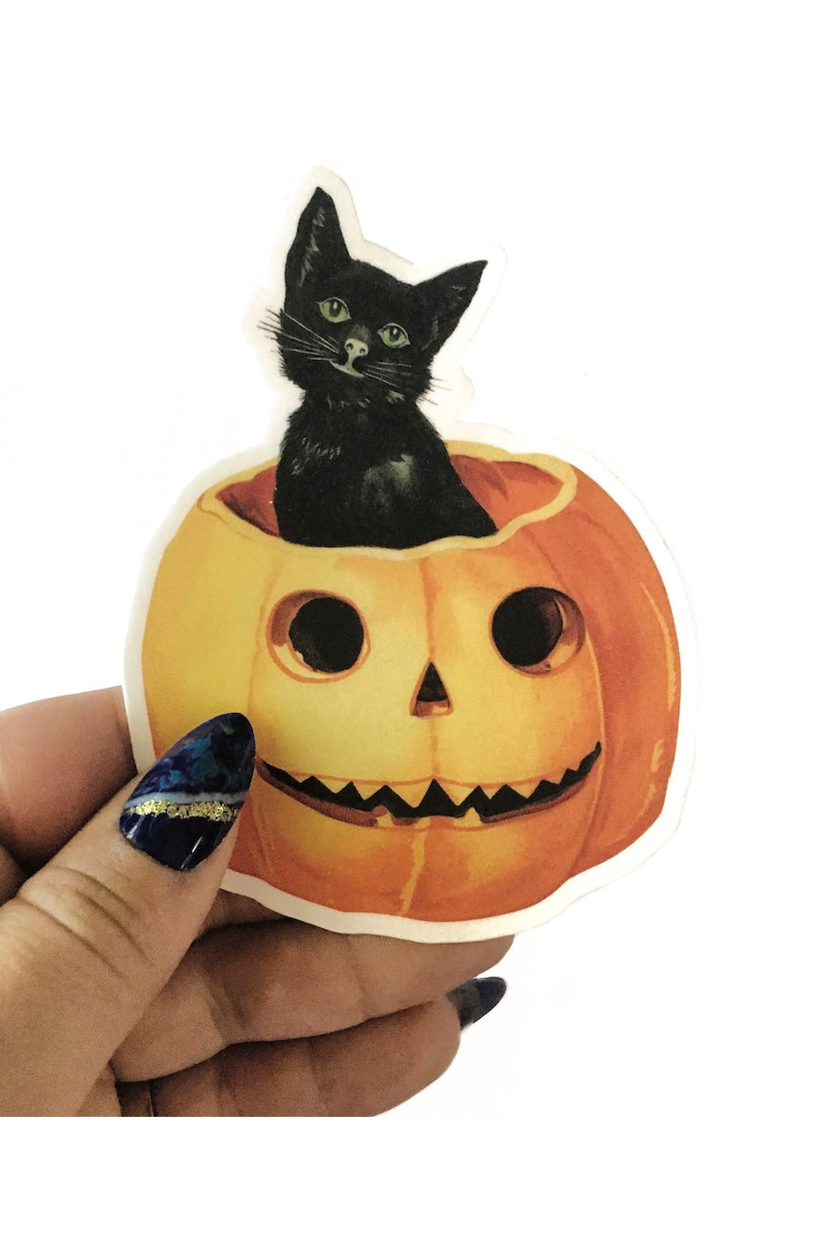 A hand holding a die-cut sticker featuring a black cat sitting inside a carved orange pumpkin jack-o'-lantern, shown against a plain white background.