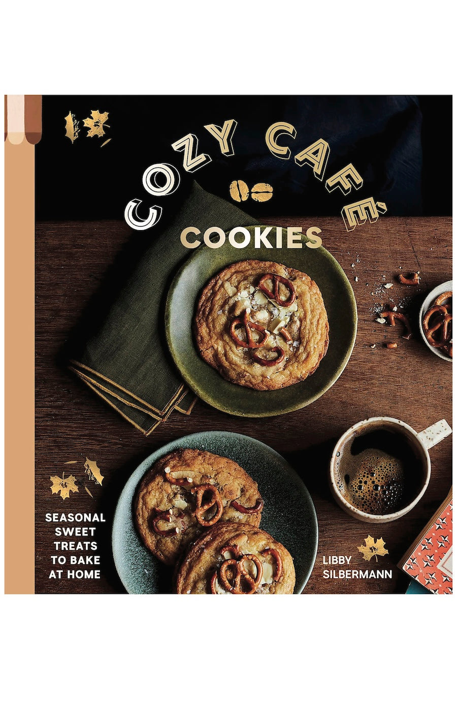 Book cover for 'Cozy Cafe Cookies' by Libby Silbermann, featuring a warm flat-lay photograph of two decorated cookies on plates on a wooden table, with a coffee cup and decorative text.