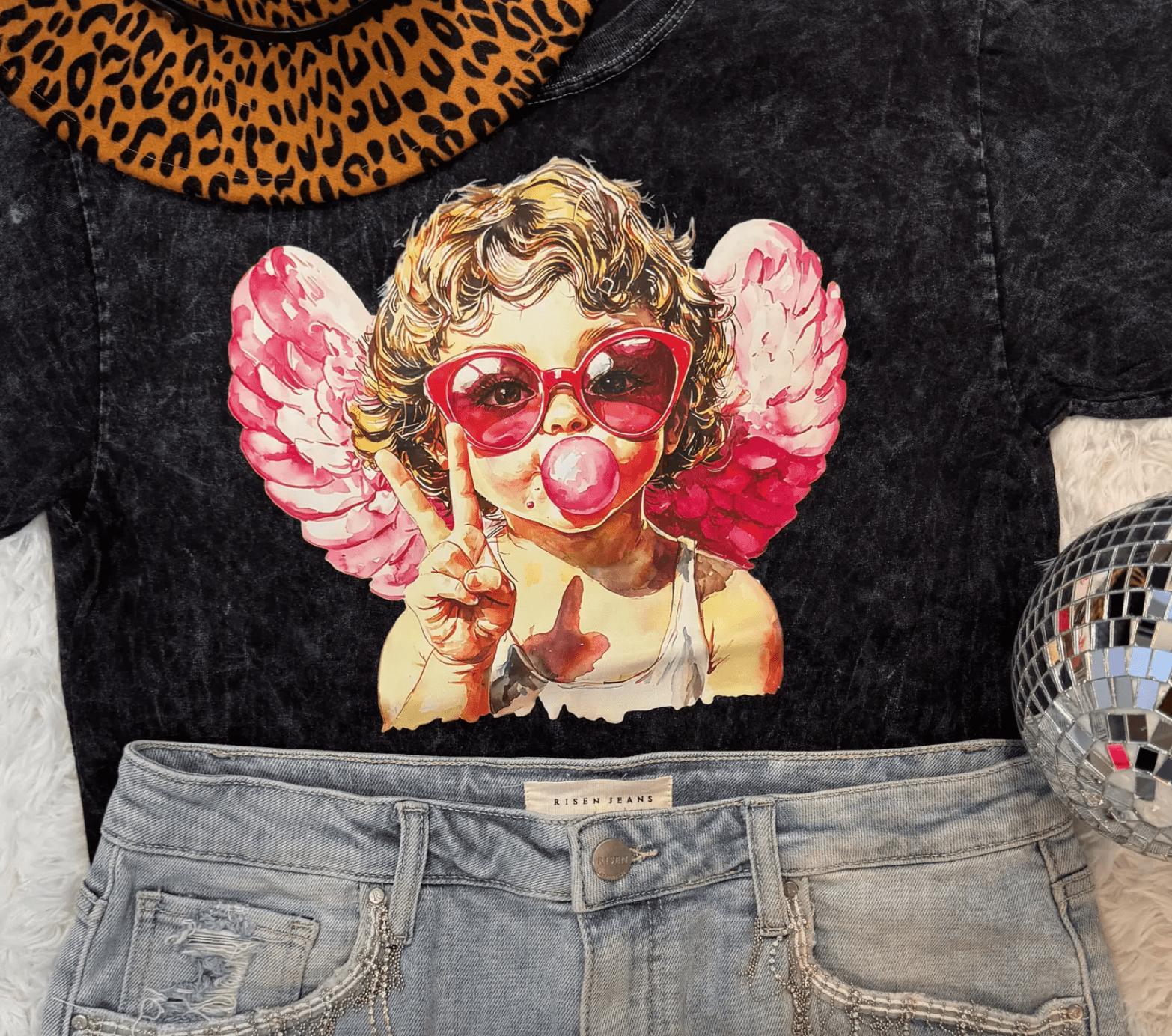 Black graphic tee with cupid blowing bubblegum and Risen Jeans denim shorts.