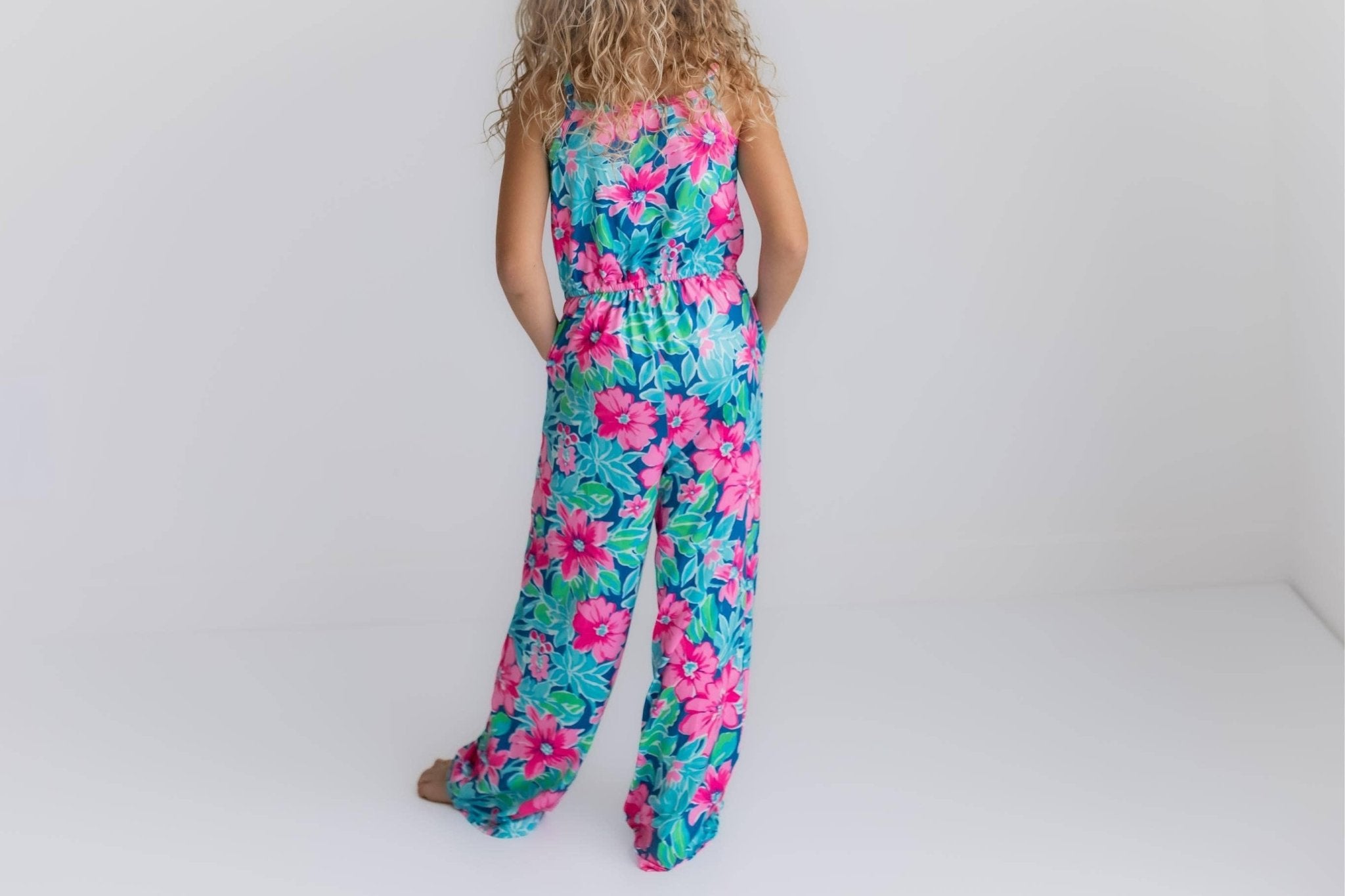 Girl in floral print jumpsuit with elastic waist and pockets. Back view.