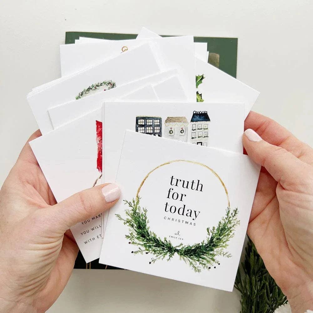 A person's hands holding a fan of white Christmas greeting cards. The front card features a green pine wreath and gold circle with the text 'truth for today CHRISTMAS'.