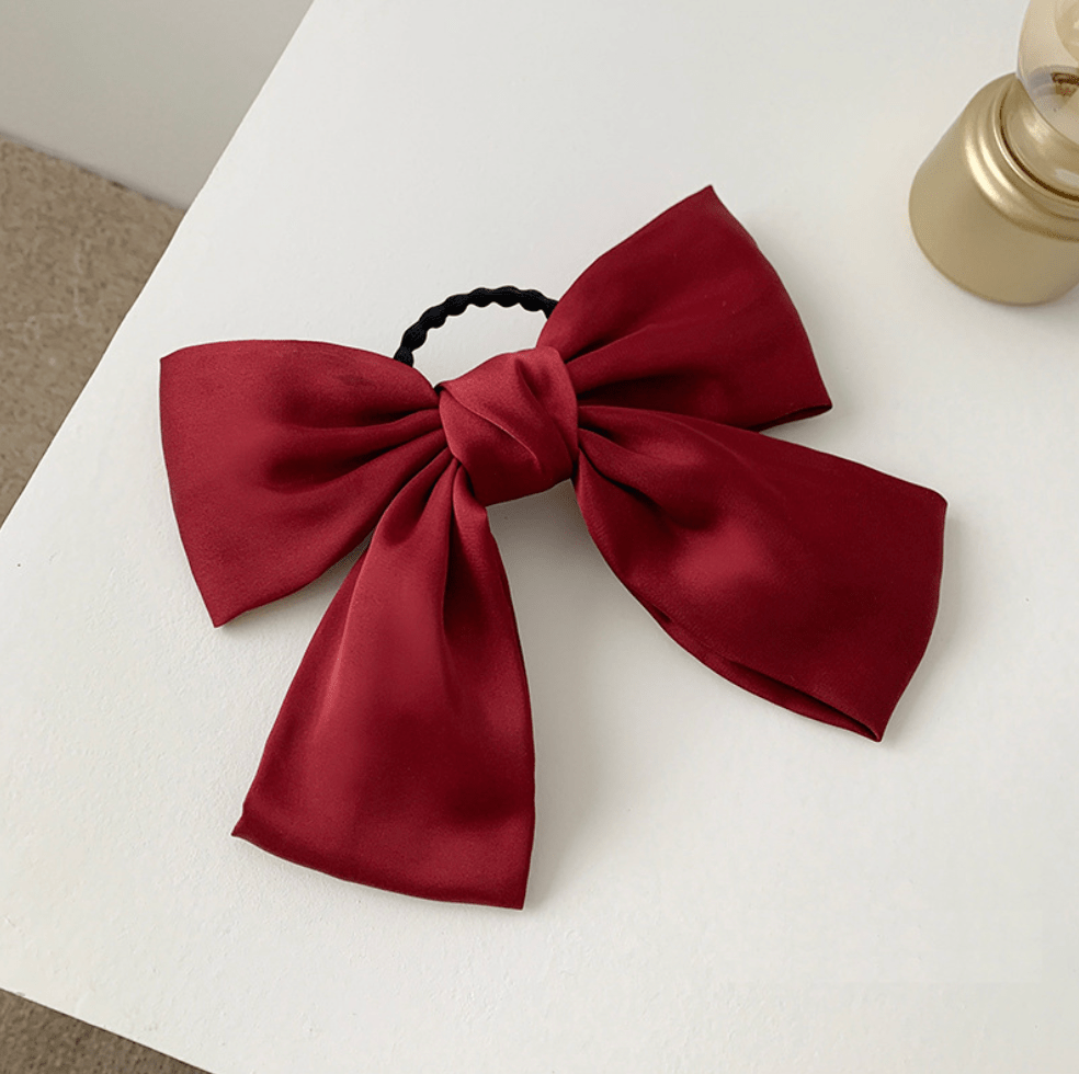 Burgundy satin bow hair tie on a white surface.