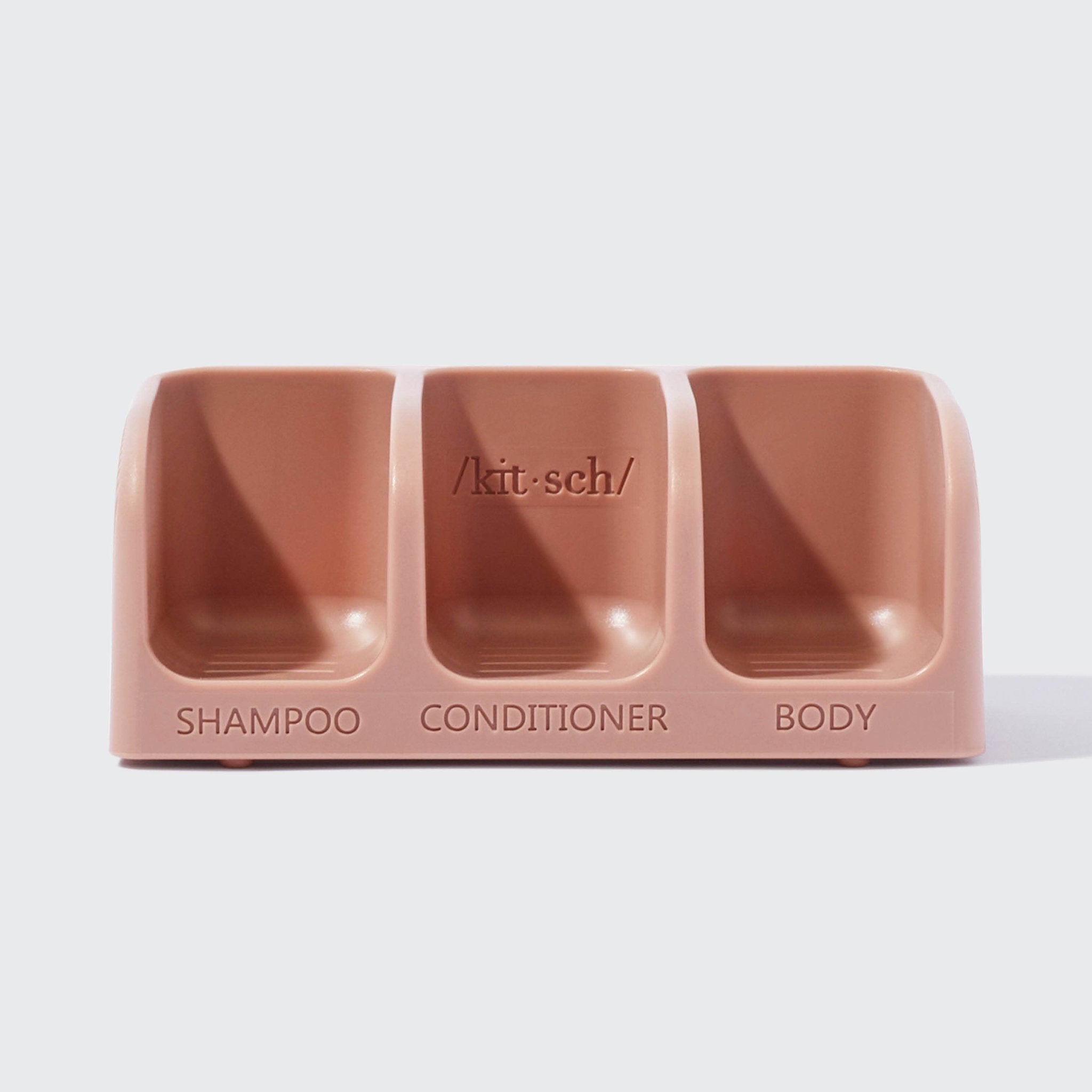 Kitsch blush pink silicone shower caddy with three slots labeled shampoo, conditioner, and body.
