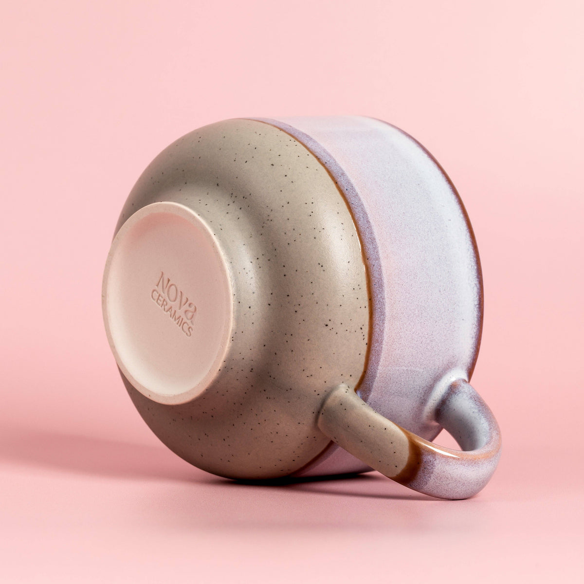 Speckled ceramic cup with a light pink interior on a pink background, featuring the Nova Ceramics logo.