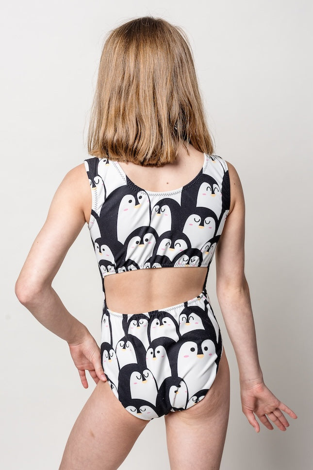 gymnast wearing a black and white penguin-patterned open-back tank leotard on a plain background
