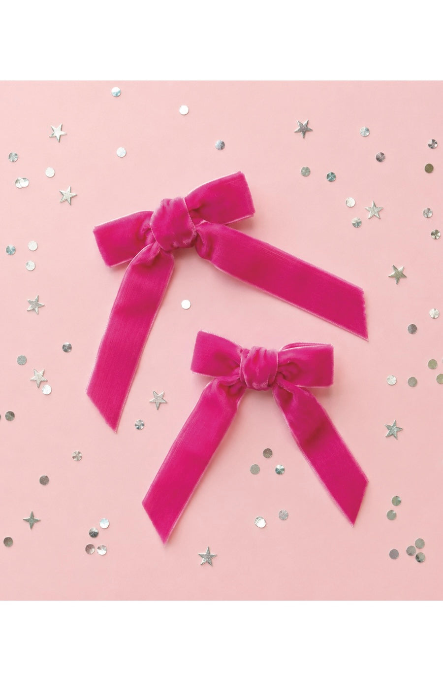 Two bright pink velvet ribbon bows of different sizes arranged on a light pink background scattered with silver star and circle confetti.