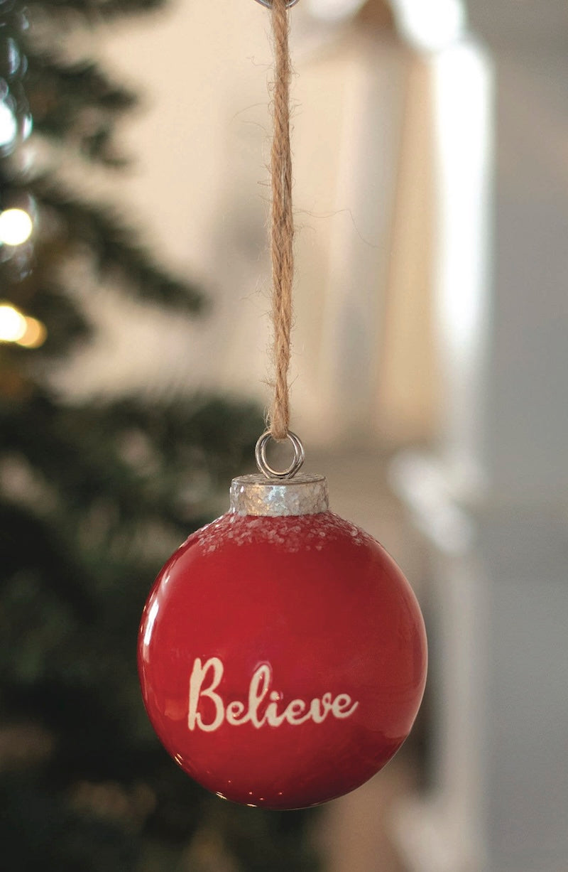 Red Christmas ornament with 'Believe' text hanging against a blurred festive background