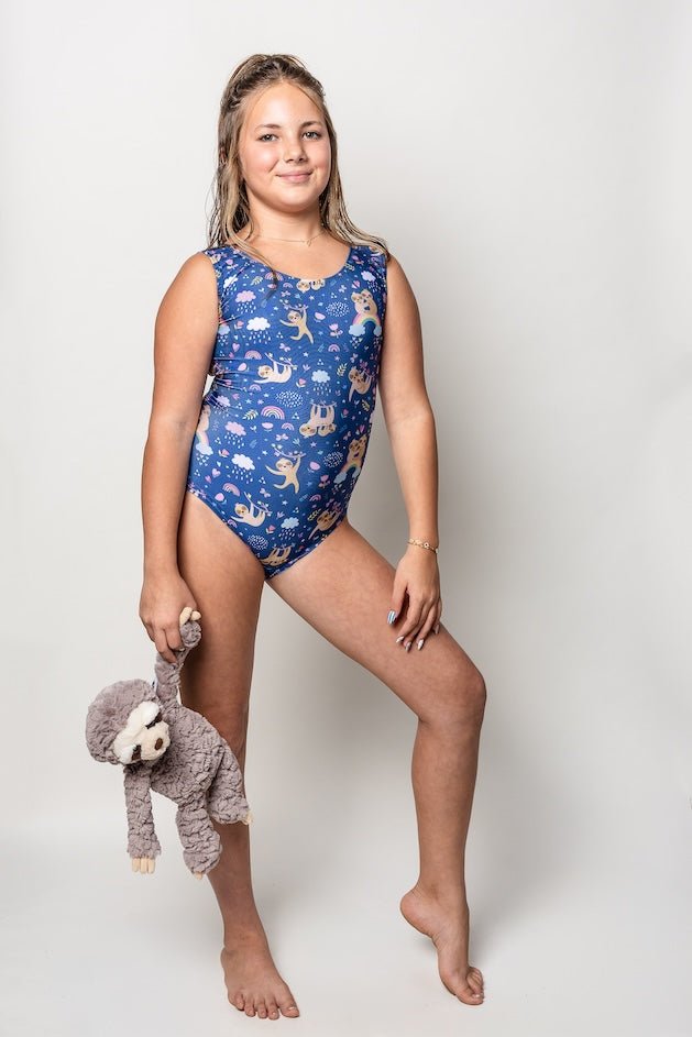 Young girl wearing a blue leotard with animal patterns, holding a sloth plush toy on a white background.