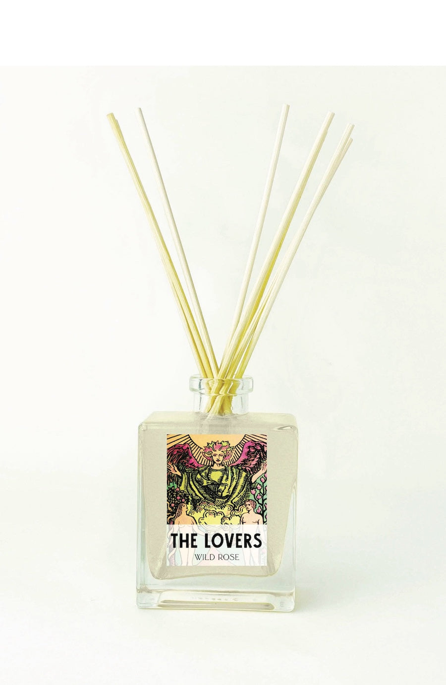 A square glass reed diffuser bottle filled with pale liquid, featuring a colorful illustrated label that reads 'THE LOVERS' and 'WILD ROSE,' with several natural reed sticks inserted above a white background.