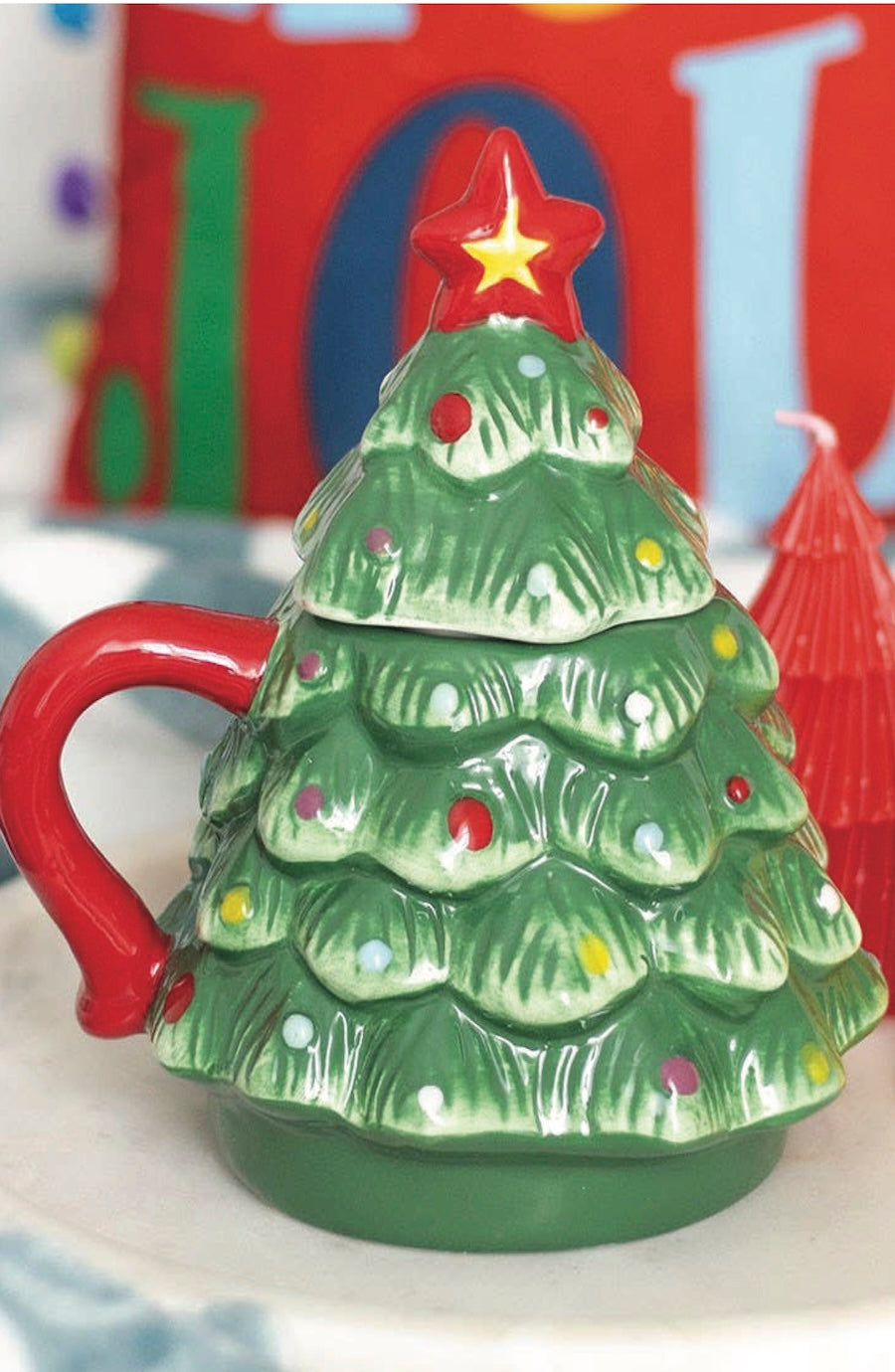 Green ceramic Christmas tree mug with red handle and star on a white surface.