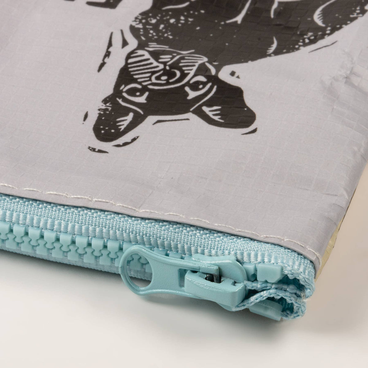 Folded fabric with a black and white cat design and a turquoise zipper on a light gray background.