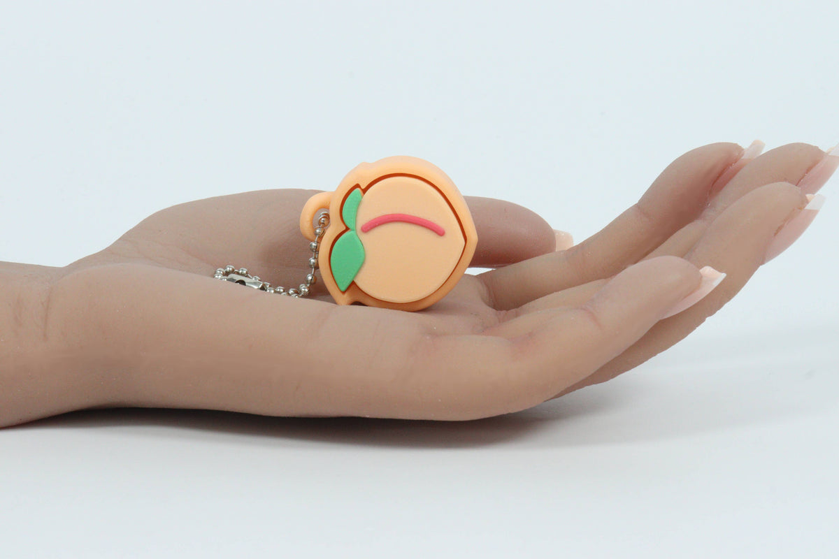 A small peach-shaped 3D-printer clicker keychain or charm with a silver ball chain resting on an open hand against a plain white background.