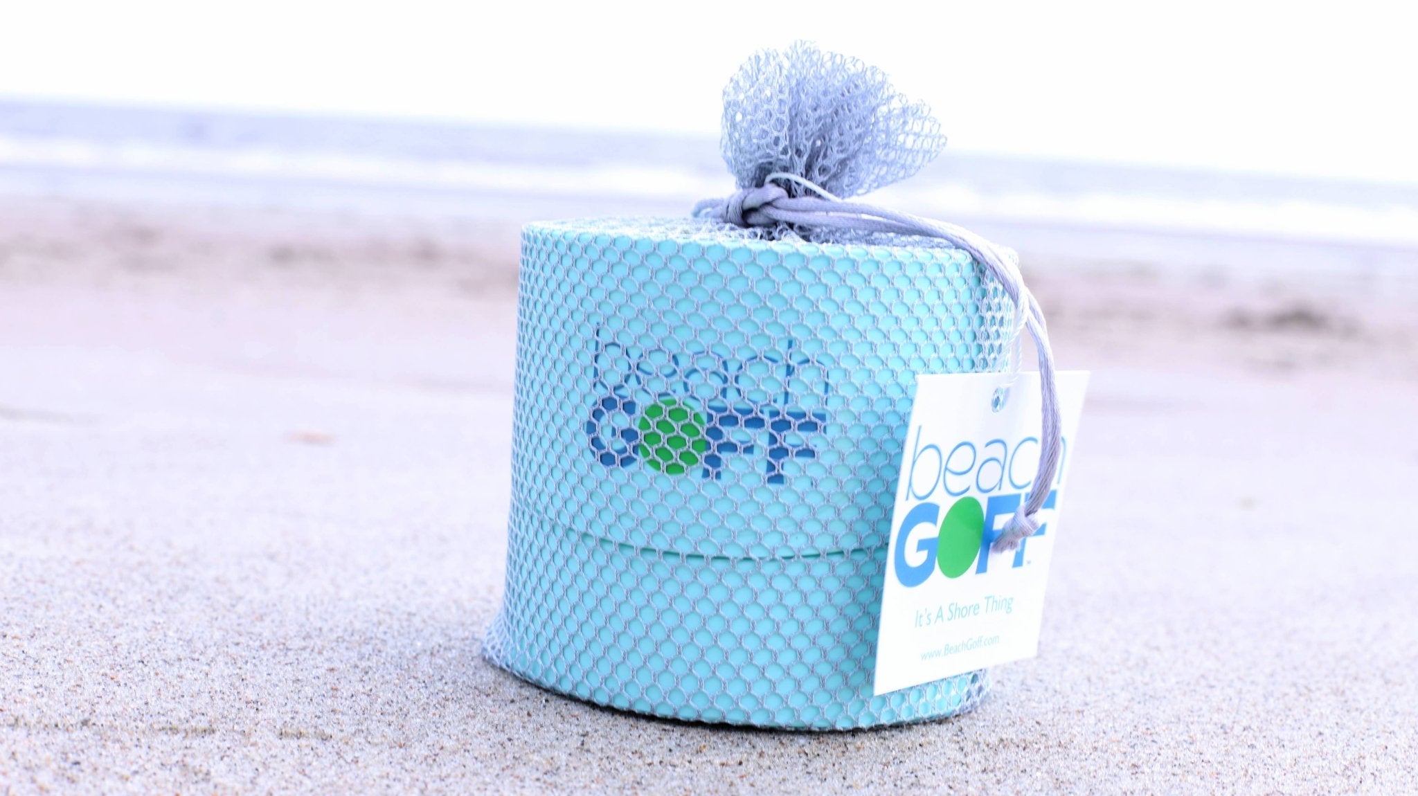 Beach GOff game set in a blue net bag, sitting on a sandy beach.