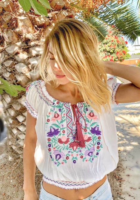 Woman wearing a colorful embroidered top with a palm tree in the background