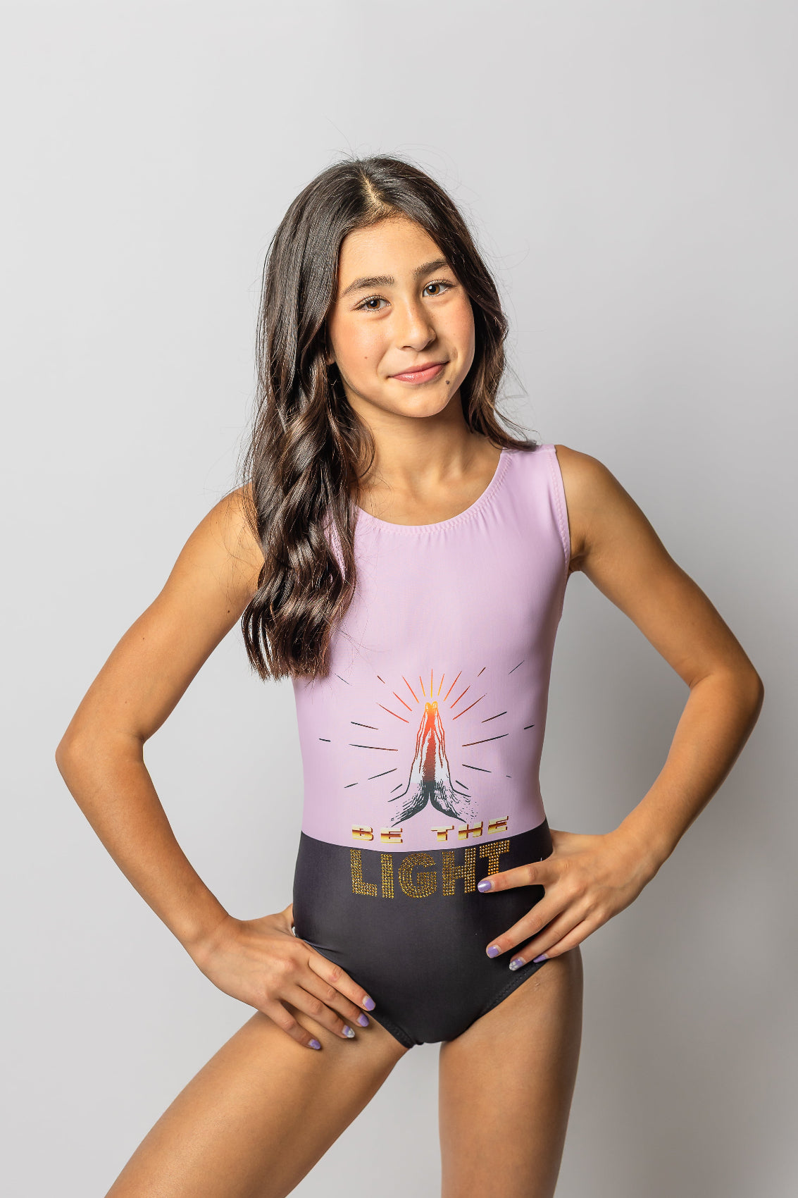 Girl wearing a pink leotard with a be the light design with prayer hands n a plain background