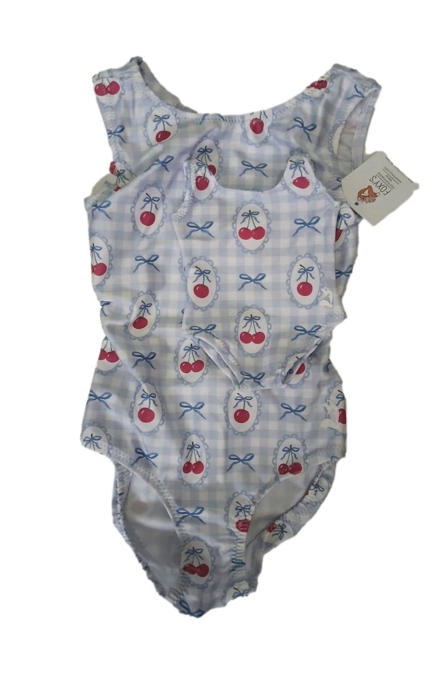 A baby leotard with matching doll leo with a light blue and white gingham pattern, decorated with red cherries and blue bows. The bodysuit has ruffled shoulder straps and a small brand tag attached to the neckline.