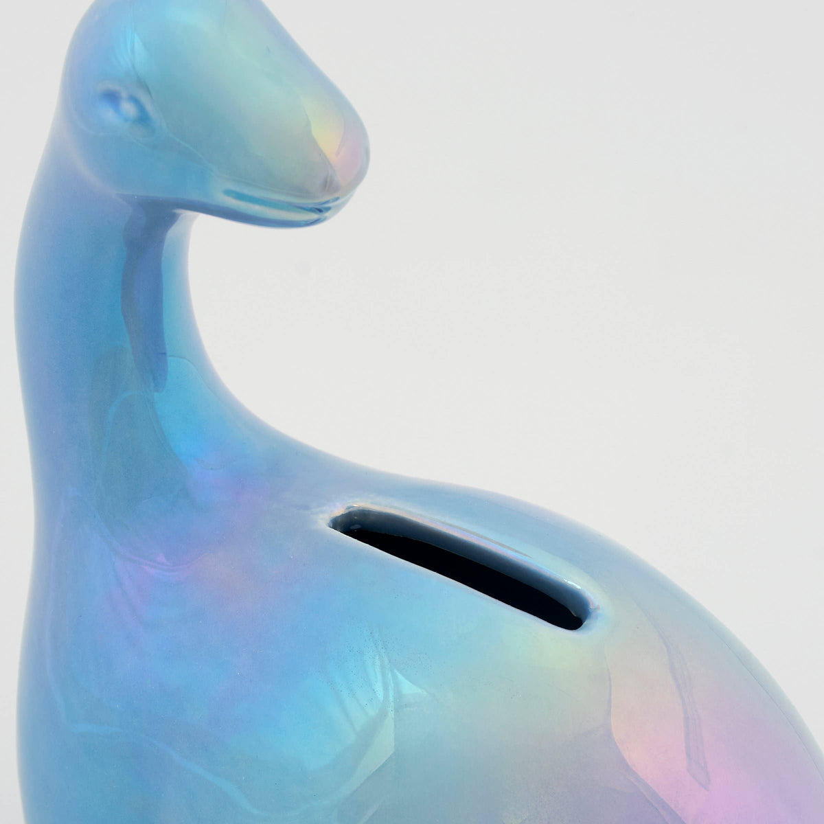 A close-up of a glossy, iridescent blue dinosaur-shaped pig bank with a slot on its back, set against a plain light gray background.