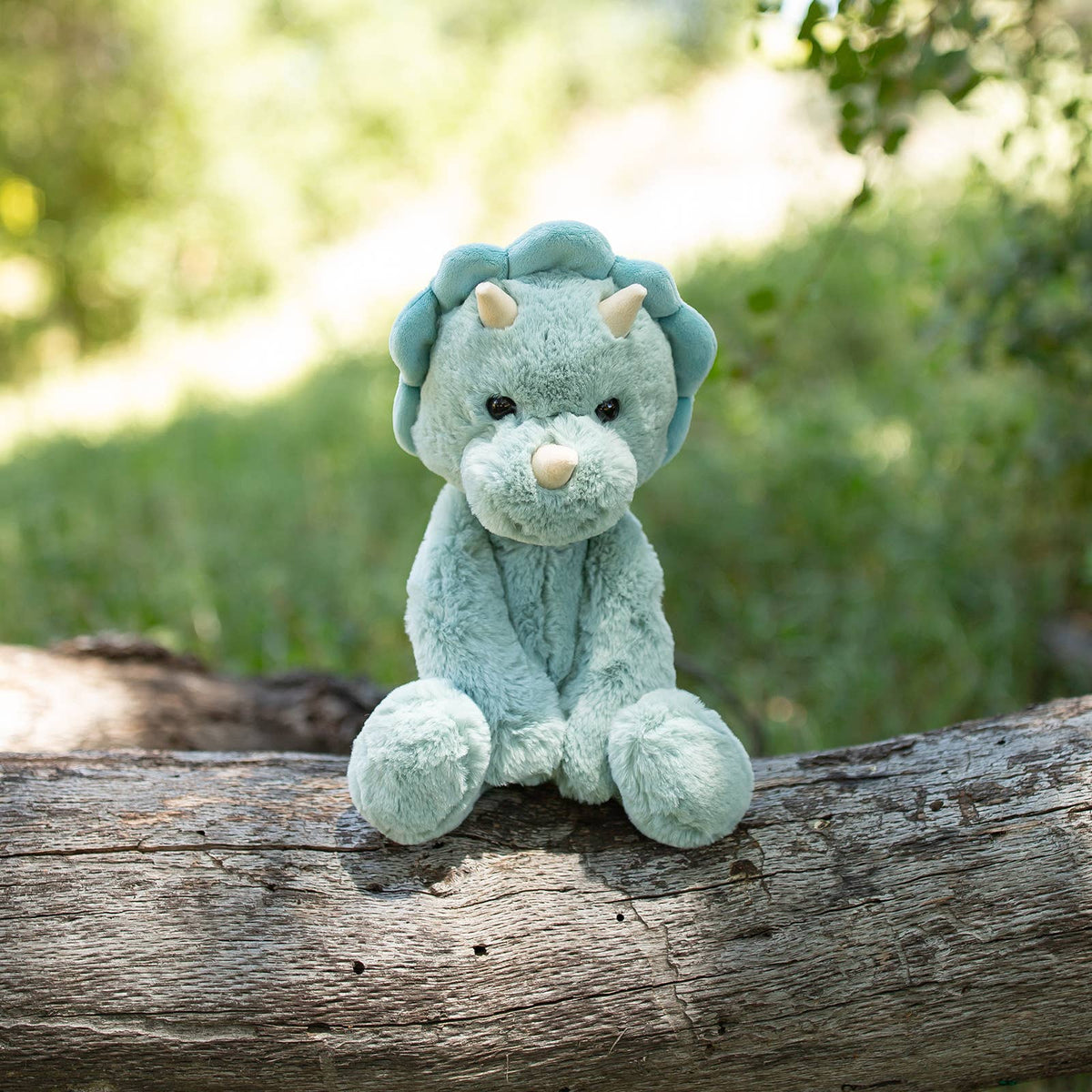 Plush dinosaur toy sitting on a log with a natural background