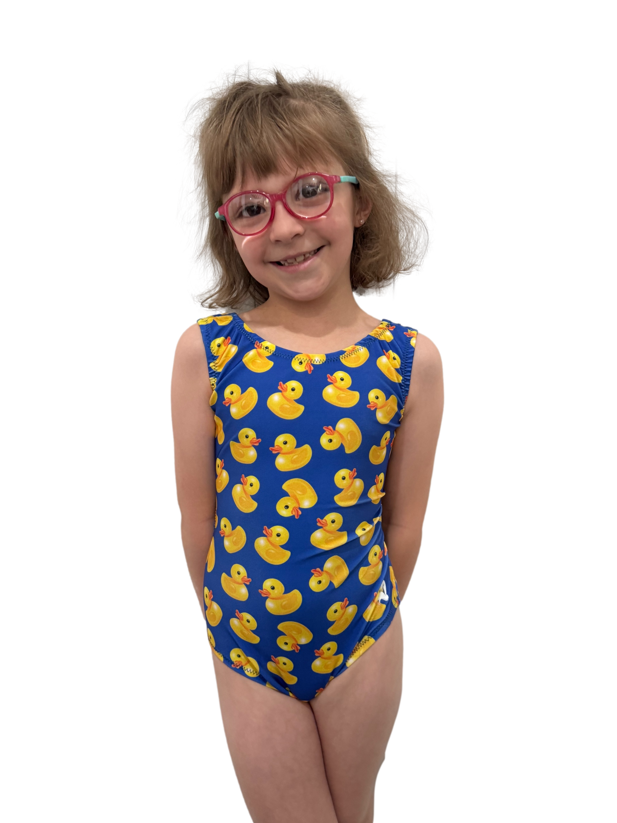 young girl wearing pink glasses and a blue leotard with a yellow rubber duck print, smiling and posing in front of a solid background